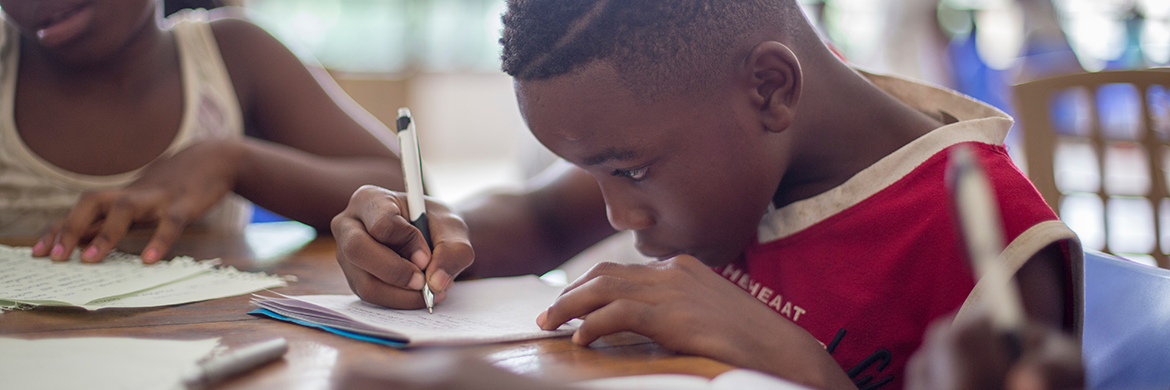 Young girl and boy sitting at a table and writing on notebook paper