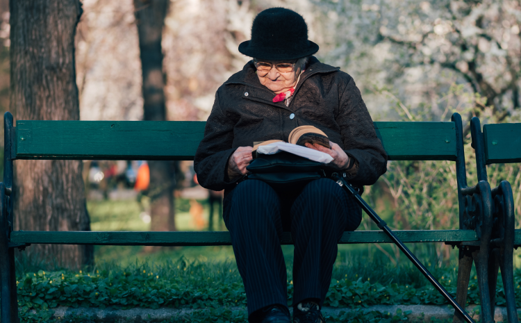 Elderly woman sitting on bench and reading